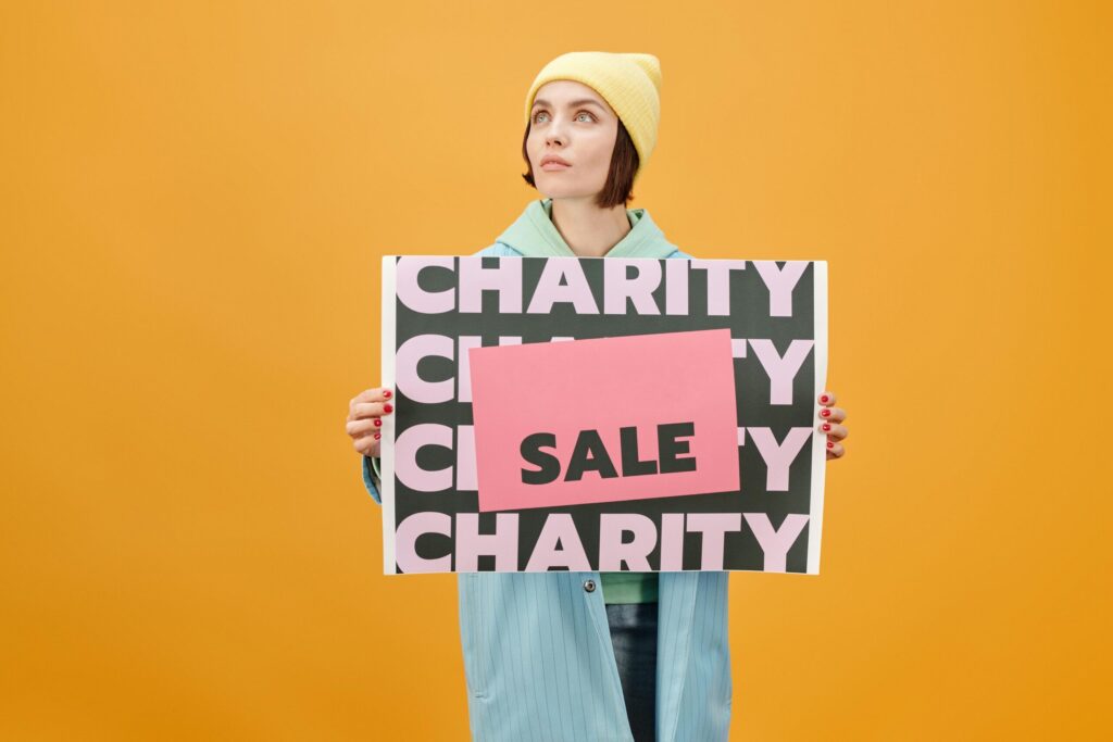 pexels-photo-5868261-5868261 Woman in trendy outfit holding a charity sale sign against a vibrant yellow background.